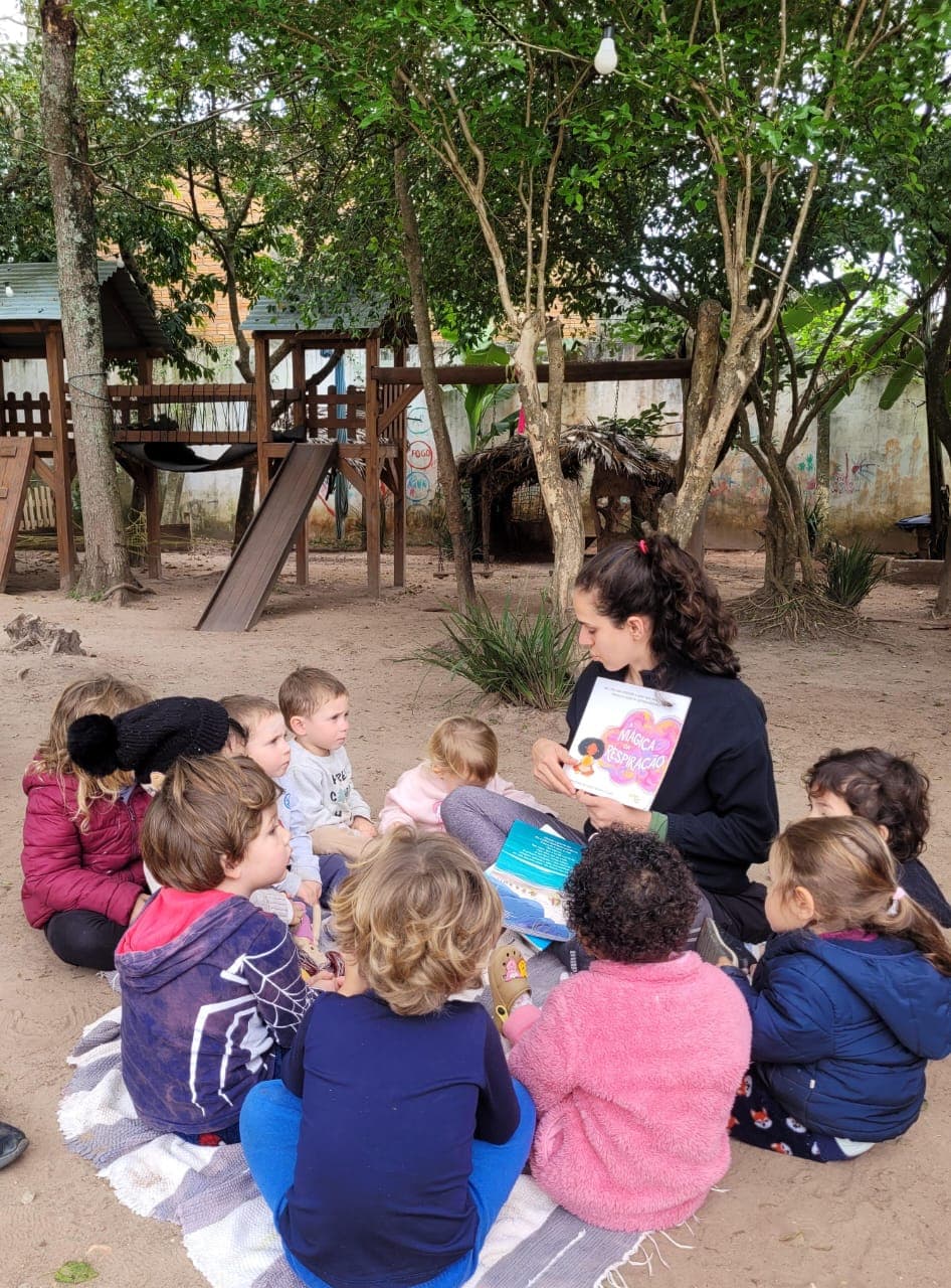 Educadora lendo um livro para as crianças sentadas em roda no pátio